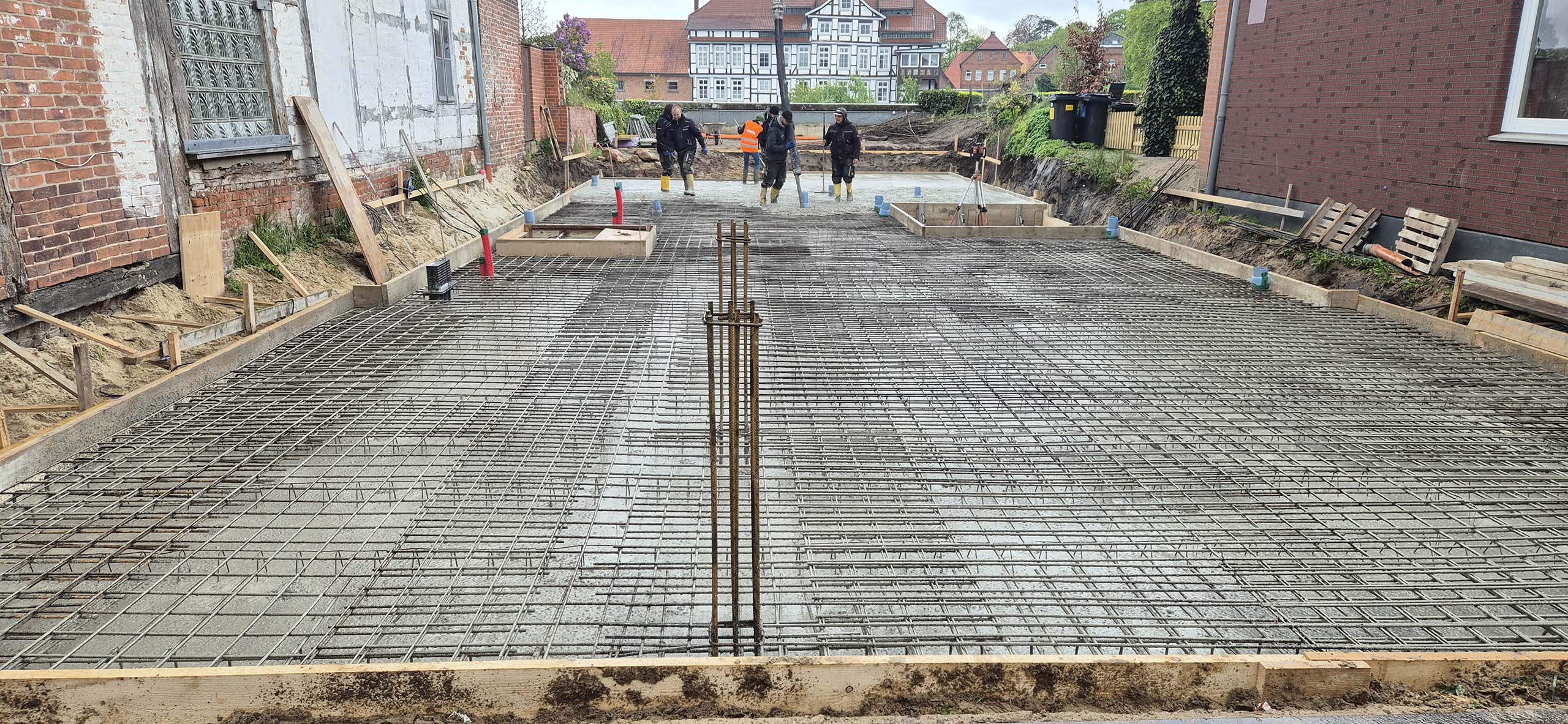 Bauprojekt in Hoya. Das verschalte Fundament mit eingesetzter Bewehrung wird von Arbeitern ausgegossen.